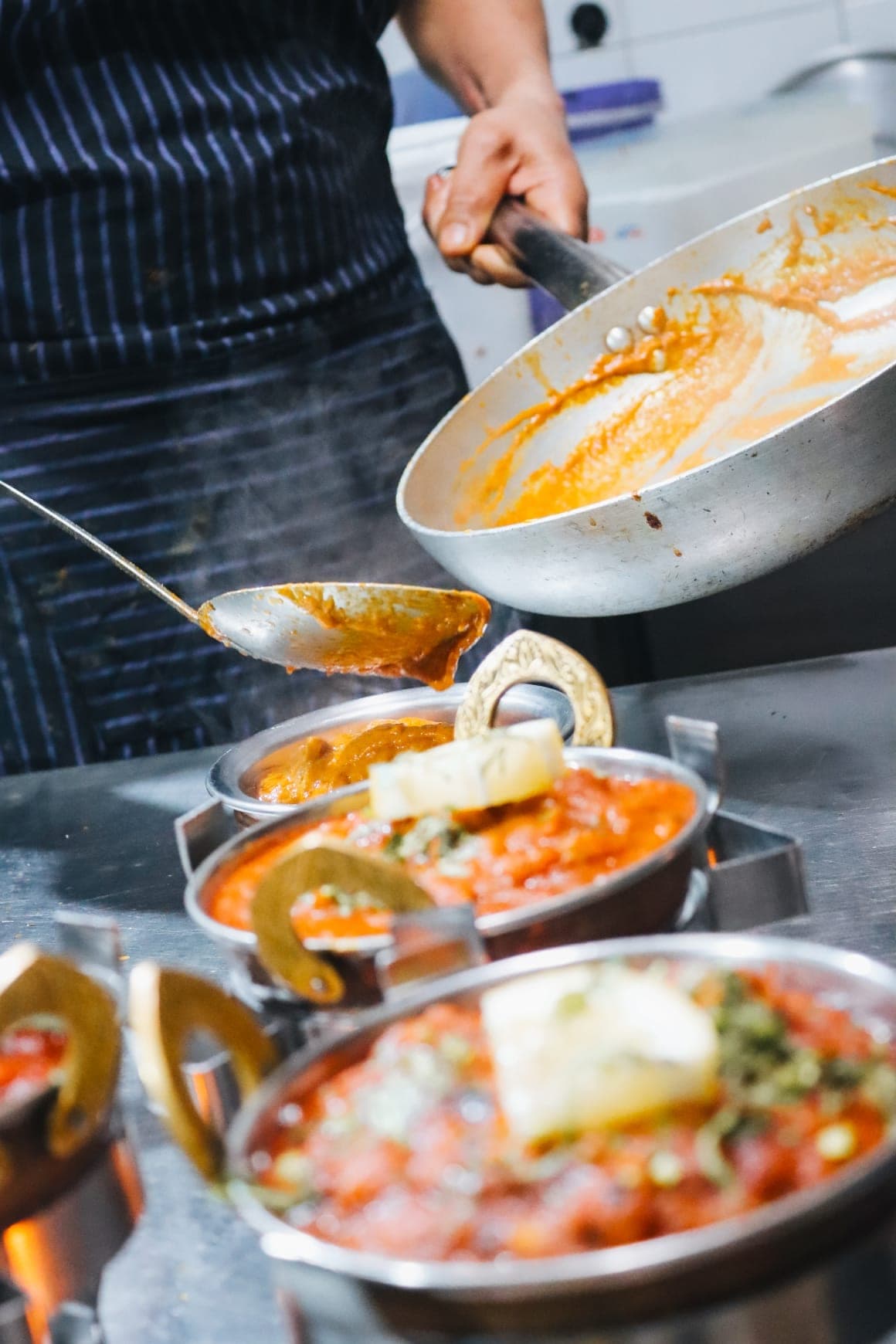 Cocinero del Indian Taj Cala Millor sirviendo salsa de curry recién hecha en cazuelas karahi – cocina india auténtica en Mallorca