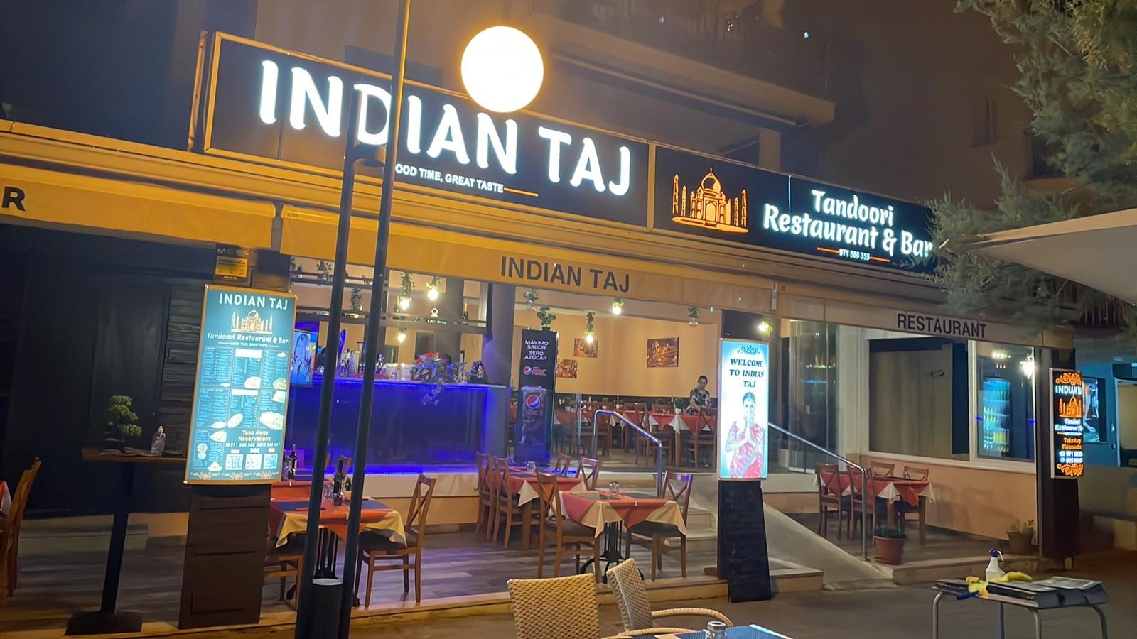 Indian Taj Cala Millor de noche – fachada iluminada del restaurante indio tandoori en el Passeig Marítim con terraza y mesas preparadas